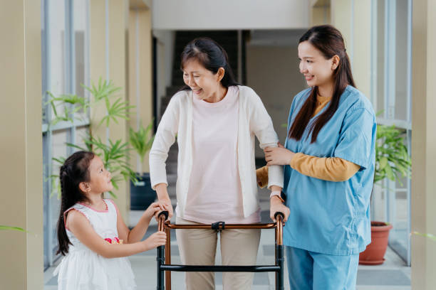 A support worker helping an older woman walk with a frame while a young girl walks alongside them